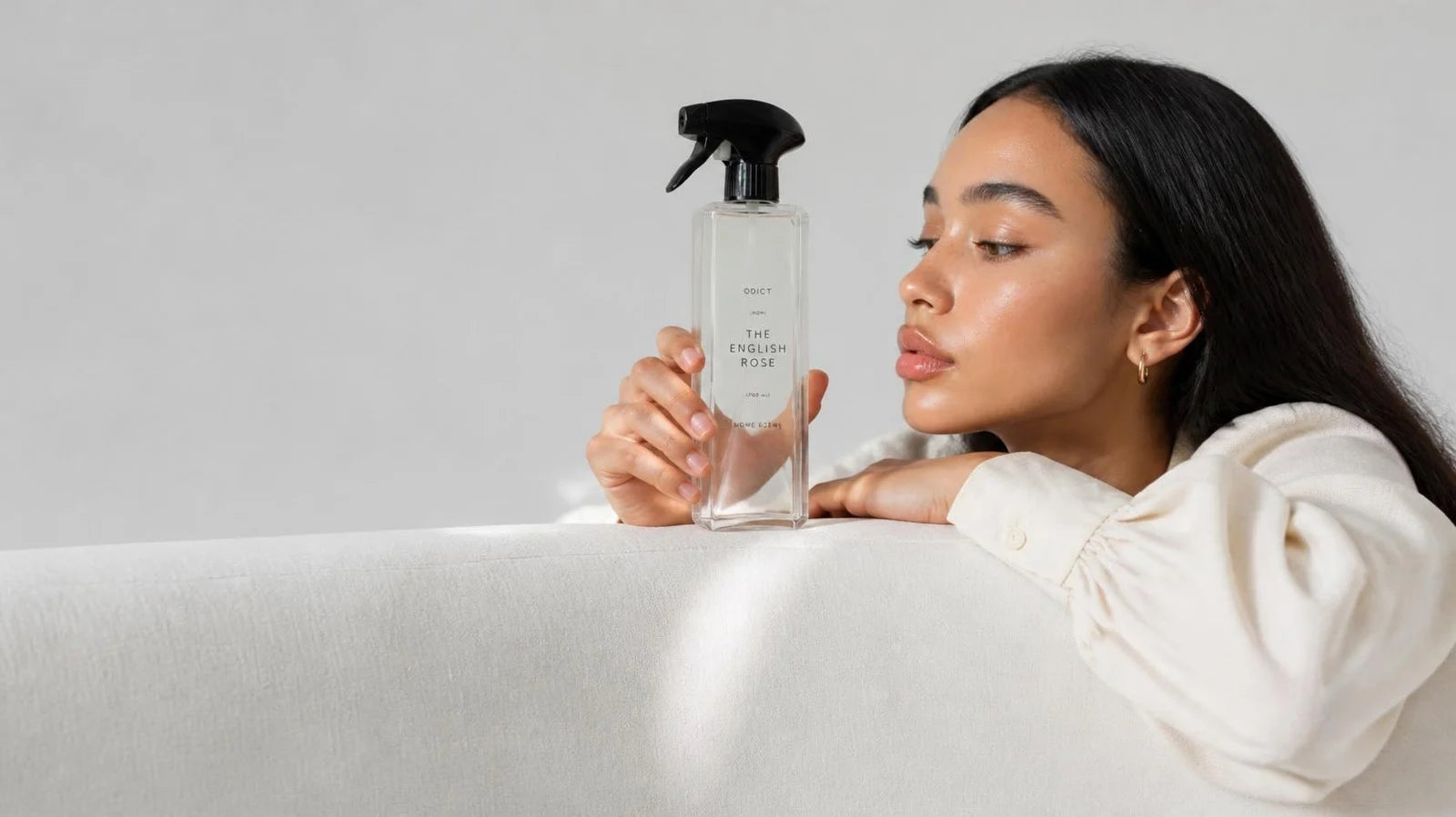 A model in an ivory top holding ODICT room spray on a sofa